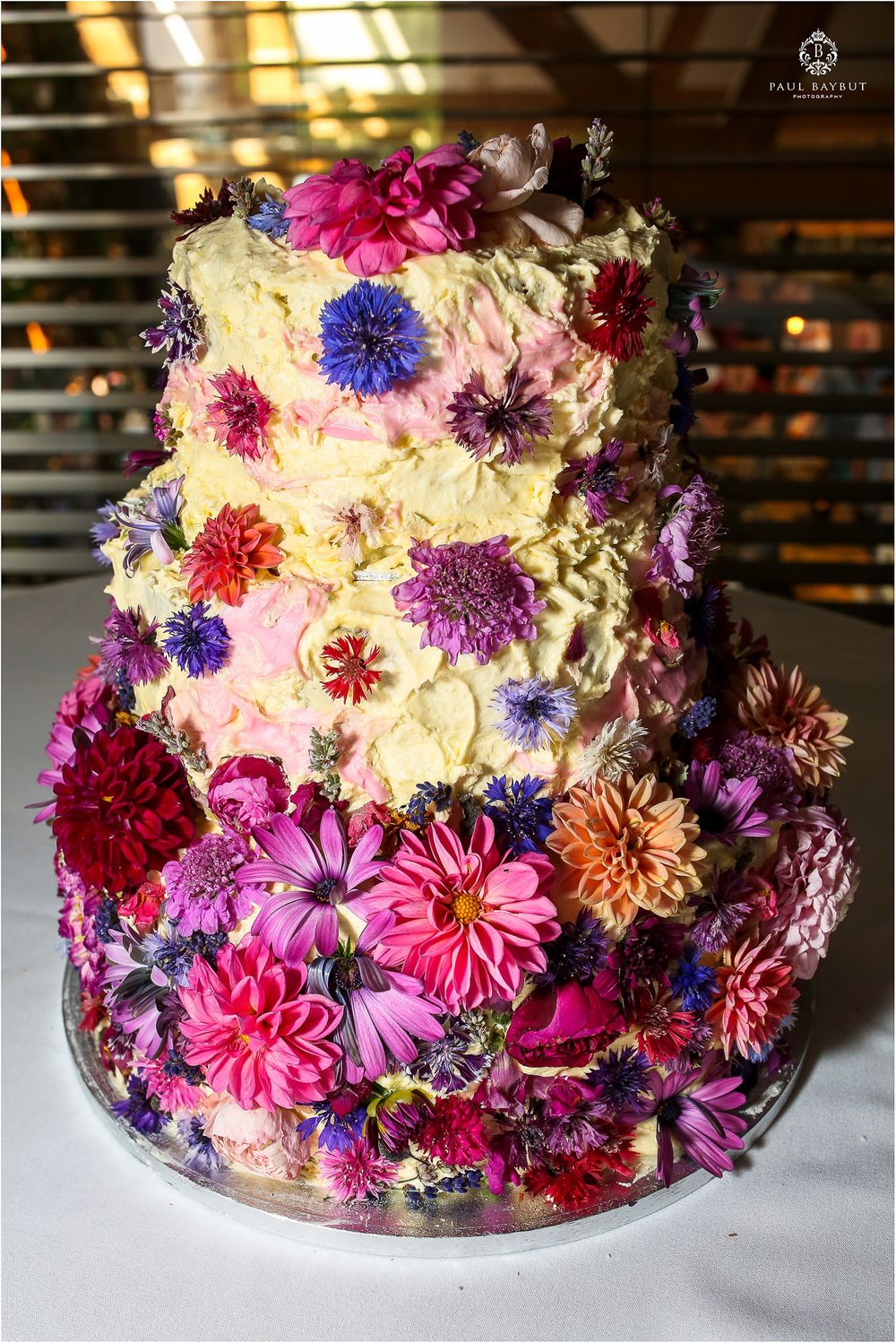 A stunning three-tier wedding cake decorated with vibrant pink, purple, and blue flowers.