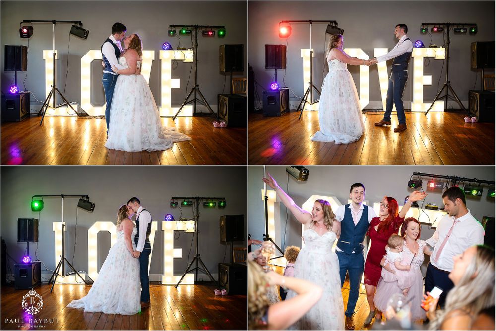 Wedding couple dancing near illuminated LOVE letters in reception venue.