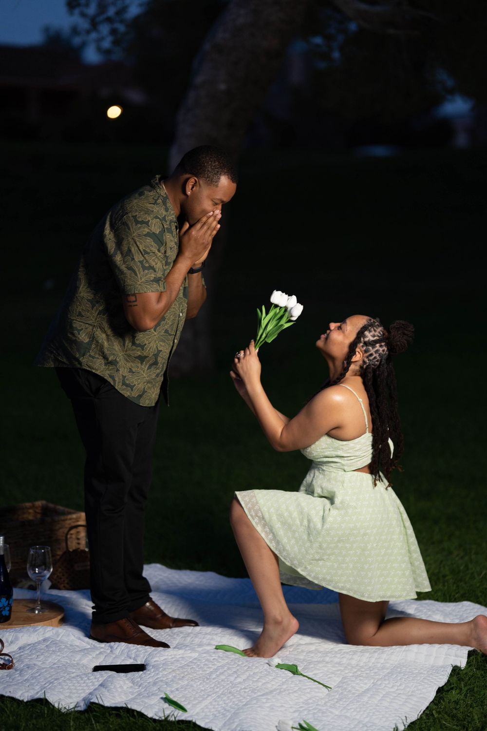 Couple sharing romantic moment during surprise proposal on picnic blanket.