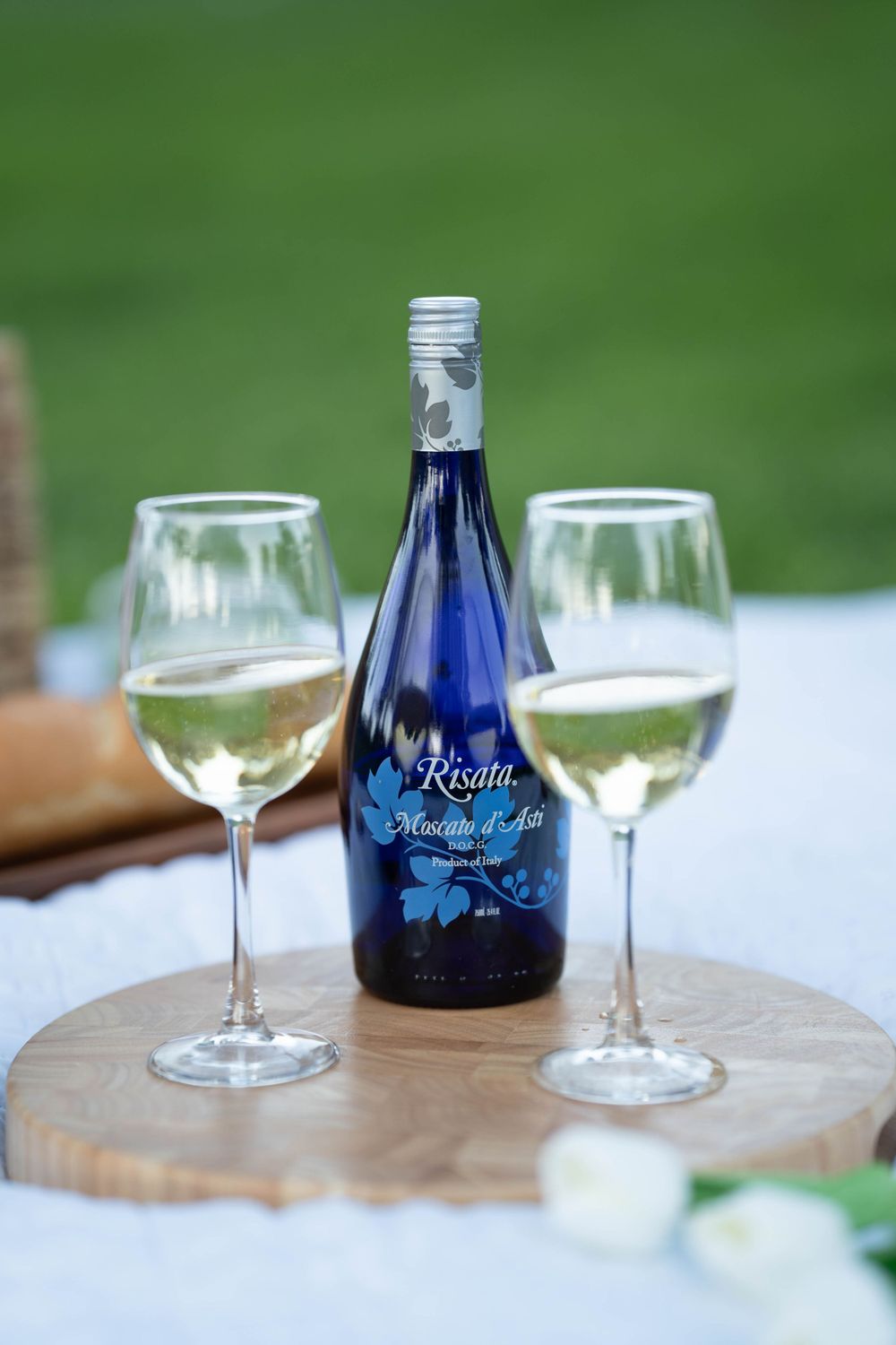 Blue wine bottle with two glasses of white wine displayed on wooden serving board.
