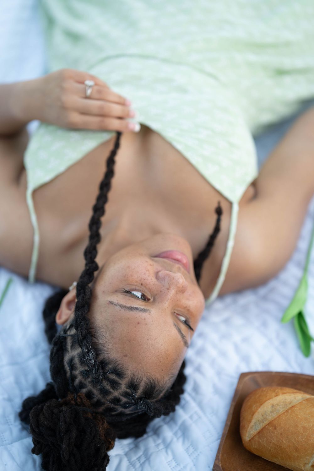 Person lying on picnic blanket next to bread and wearing mint green dress.