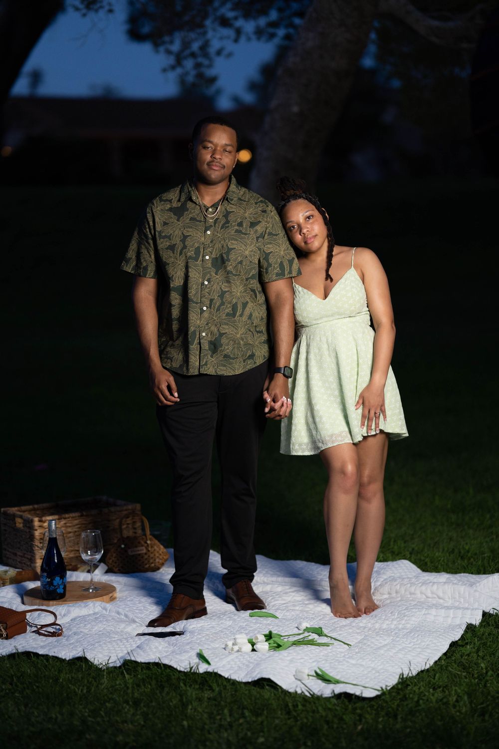 Couple standing together on white blanket during outdoor evening photoshoot.