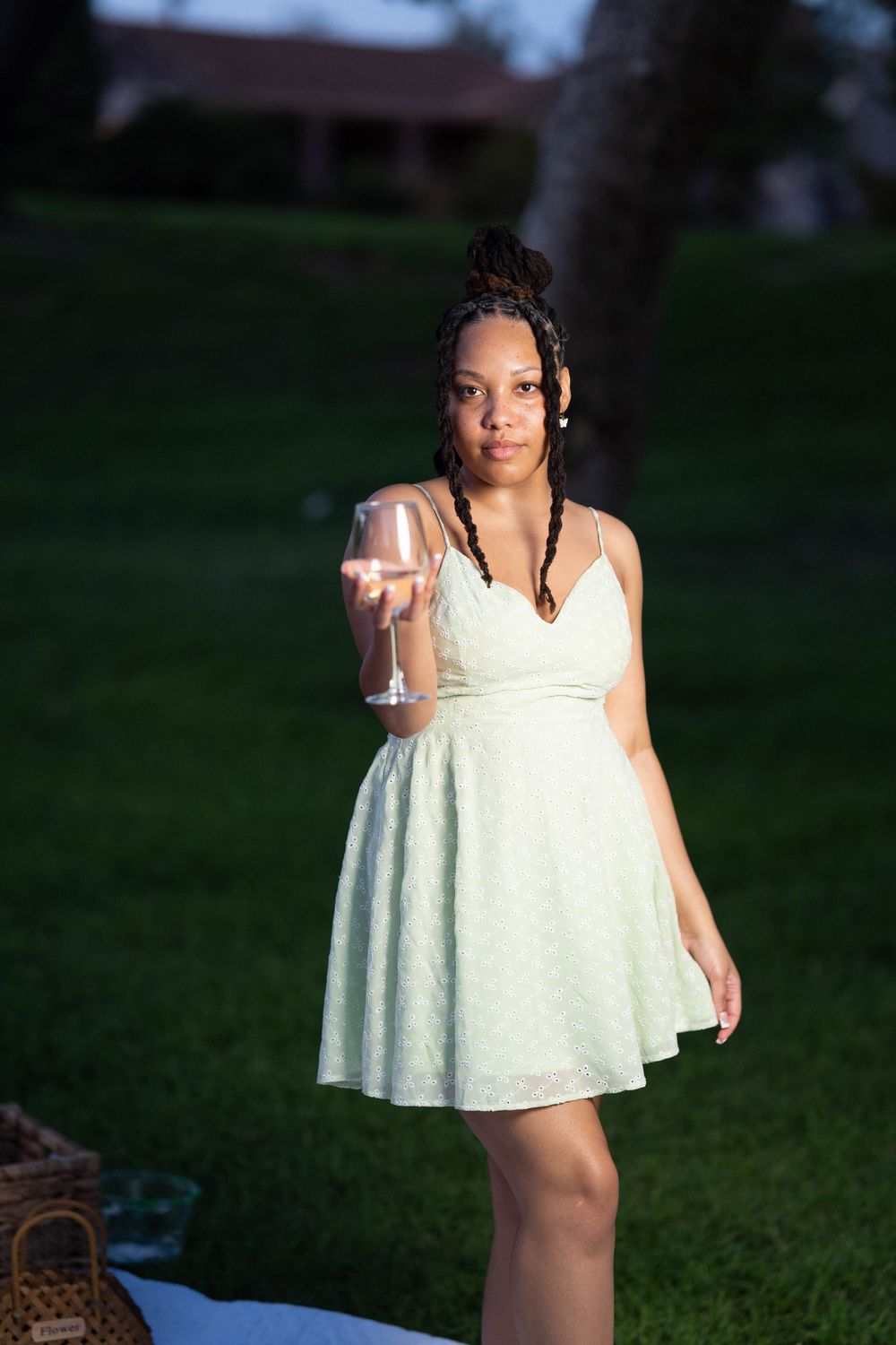 Person in white sundress holding up a champagne glass on a lawn at dusk.