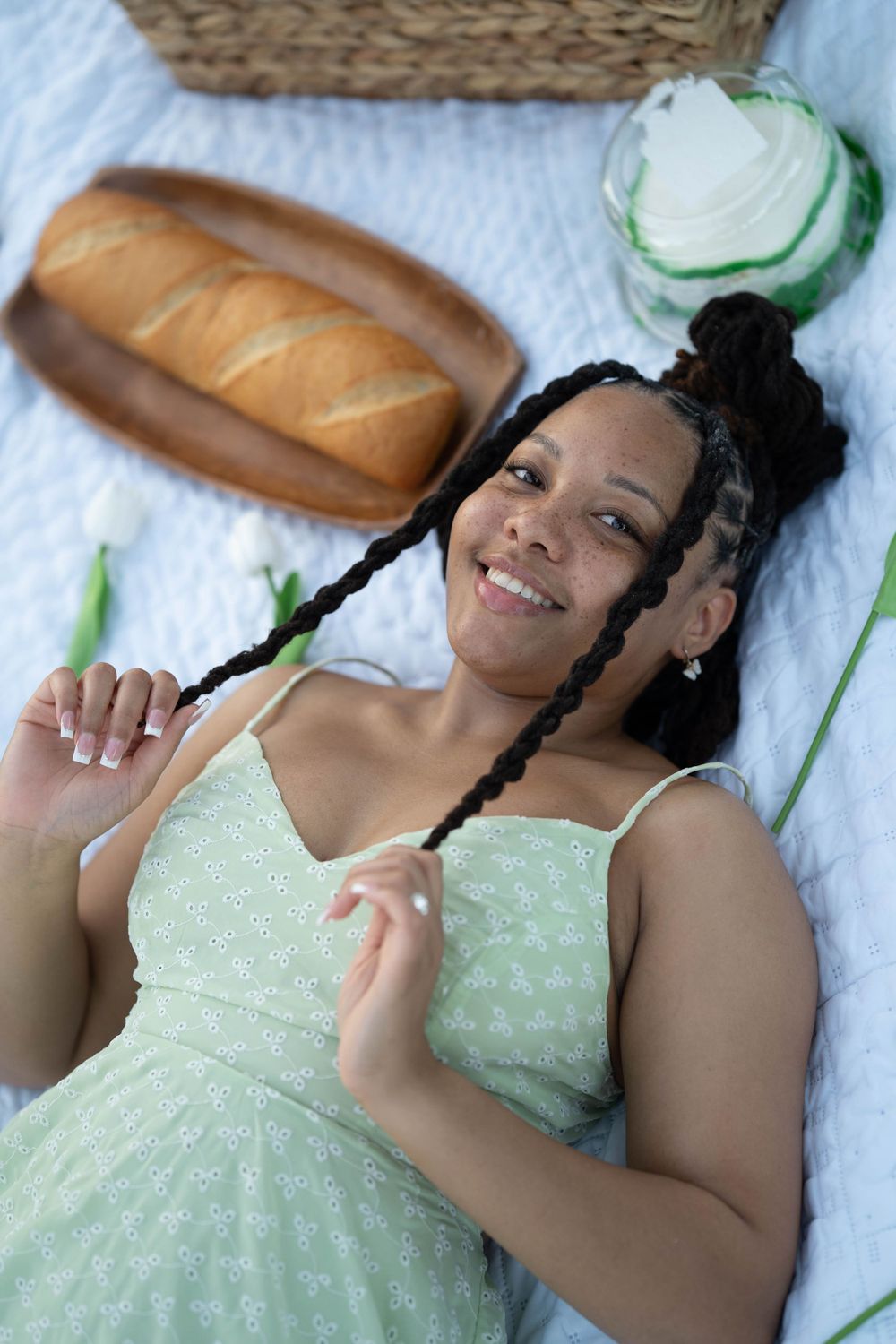 Person relaxing on white picnic blanket with braided hair and mint dress.
