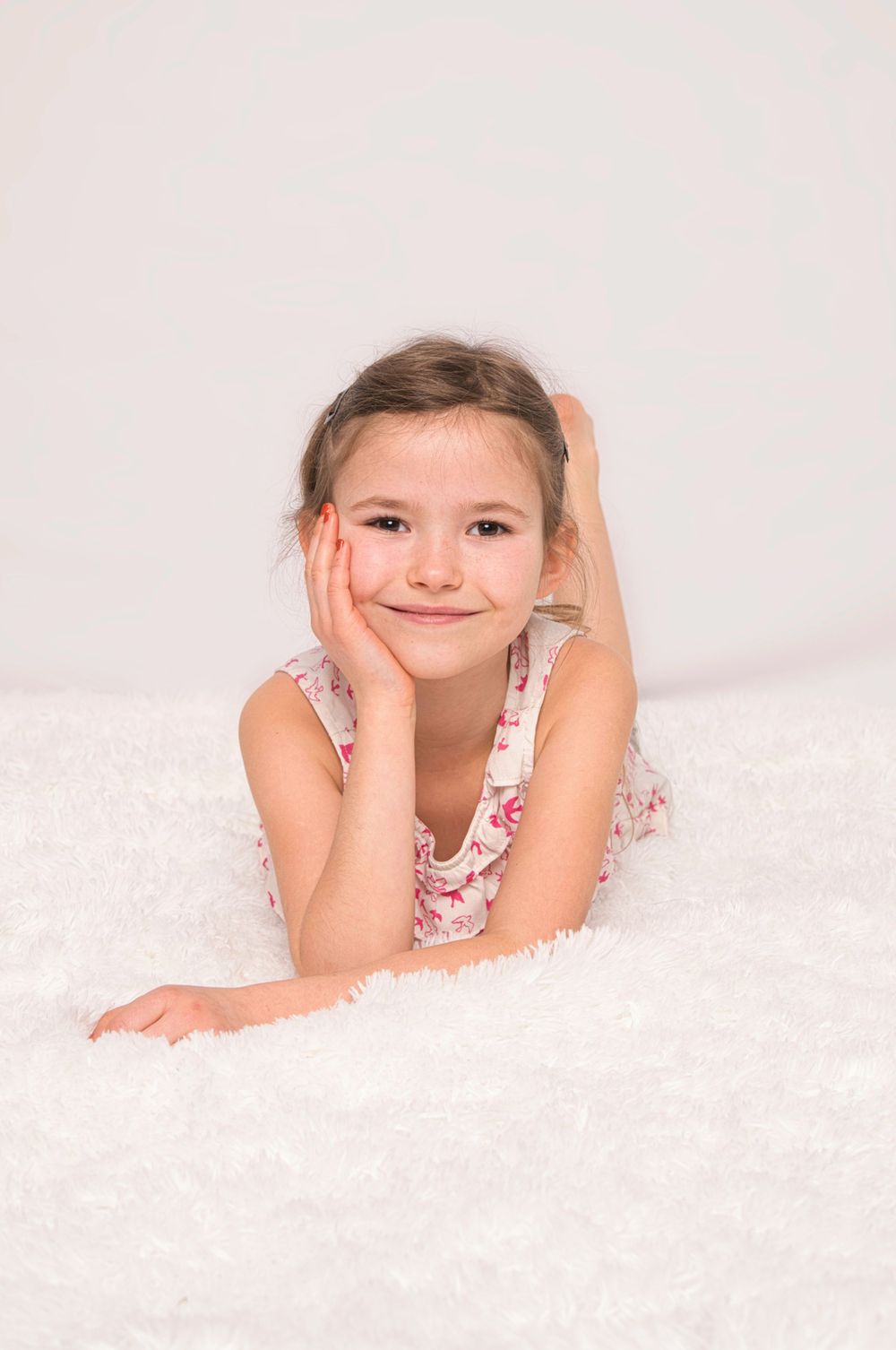 Young child in floral dress lying on white blanket during professional portrait session.