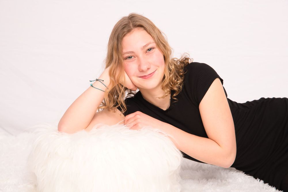 Woman in black dress relaxing on white fur during studio portrait session.