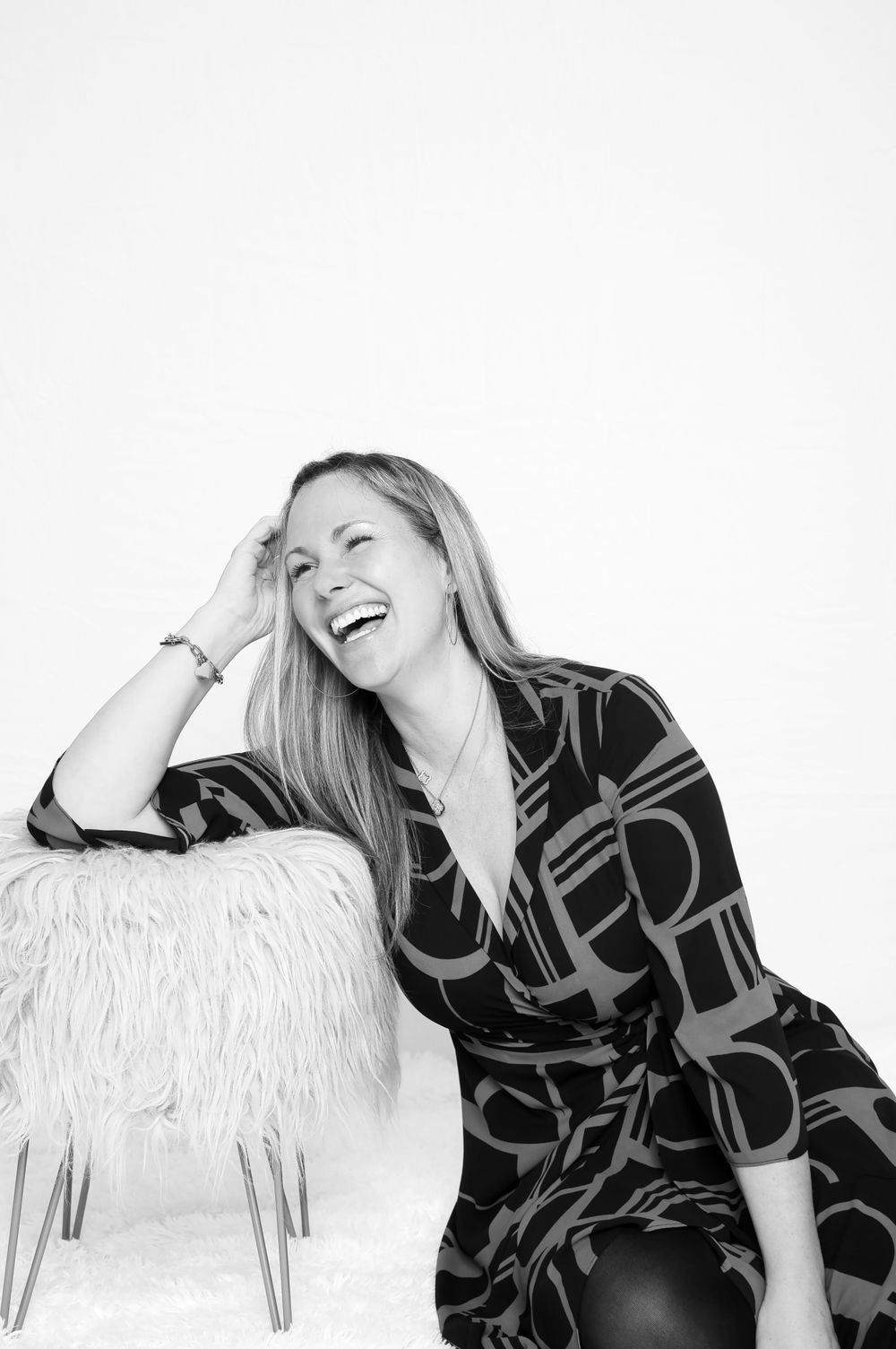 Woman in patterned dress laughing during black and white studio photoshoot.