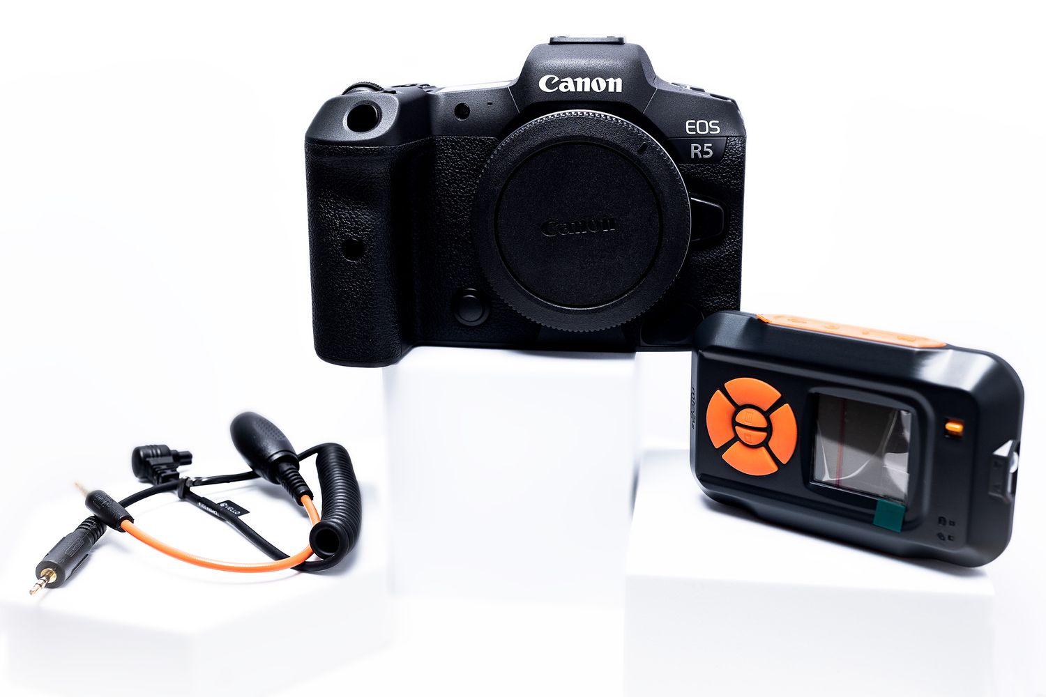 Canon R5 camera body with detached microphone and electronic trigger device on white background.