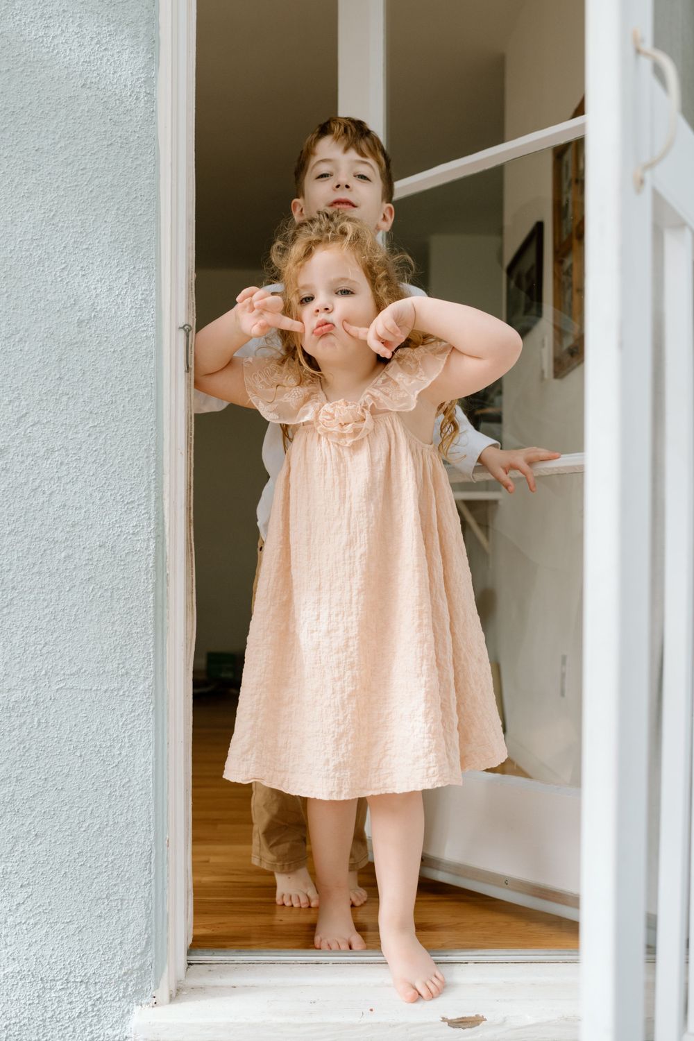Two children making funny faces while standing in a white doorway during family photoshoot in San Diego.