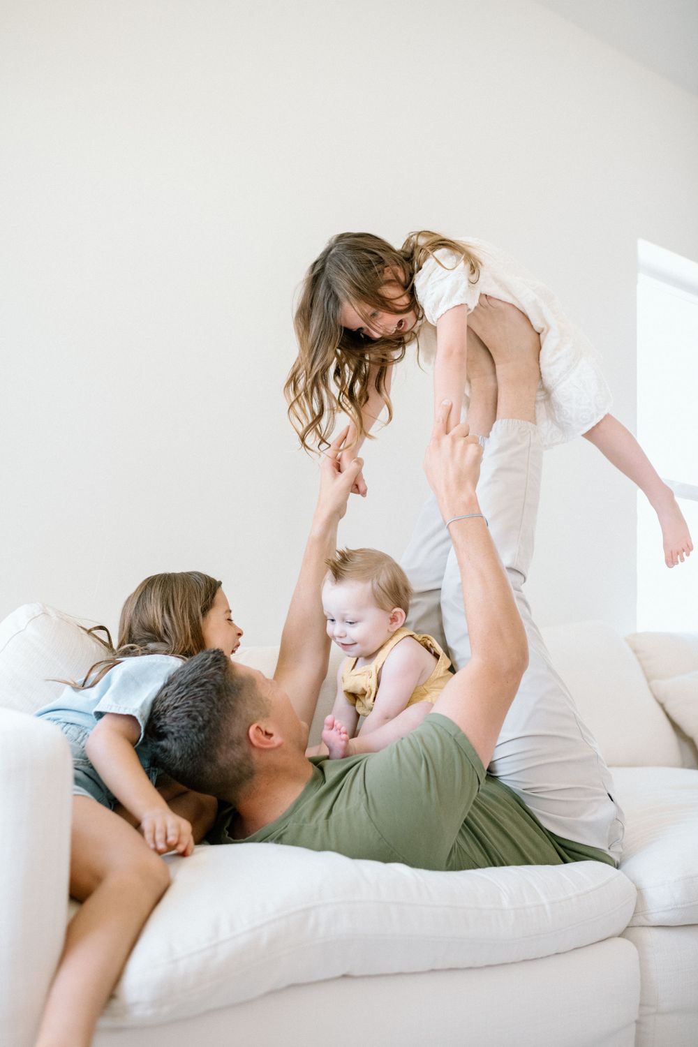 Joyful family playtime moment on white couch in bright interior during family photoshoot in San Diego.
