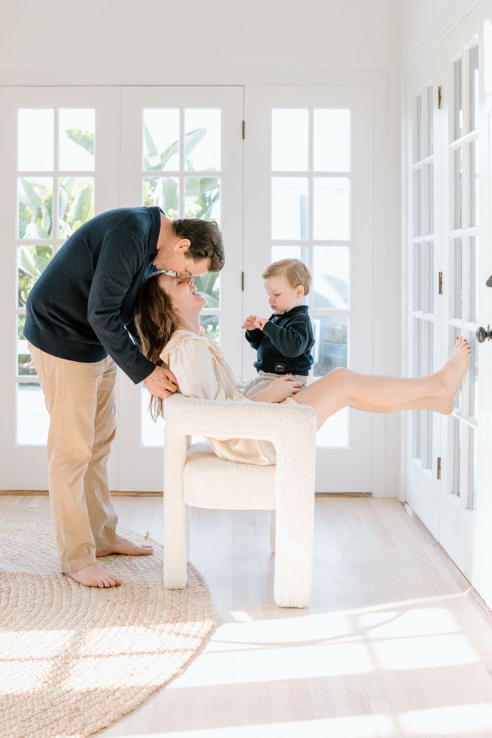Bright sunlit room with a family sharing an intimate moment on a white bench by French doors.