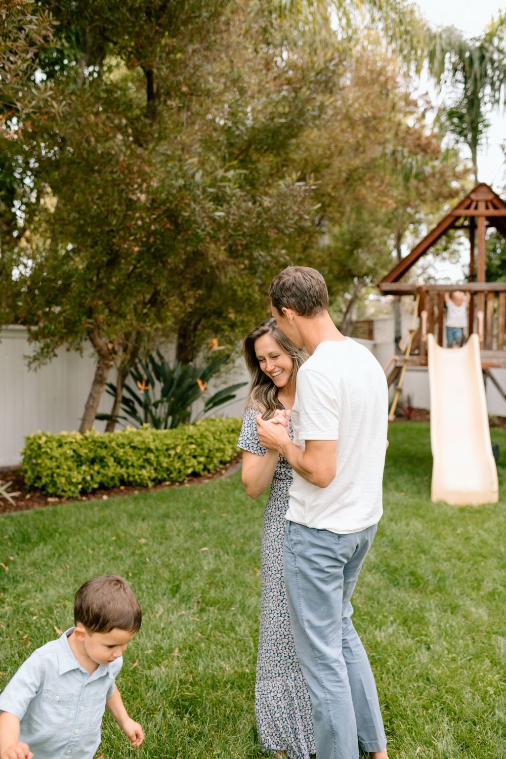 A mom and dad slow dance in the backyard while two sons run around them during a family photoshoot in San Diego, CA