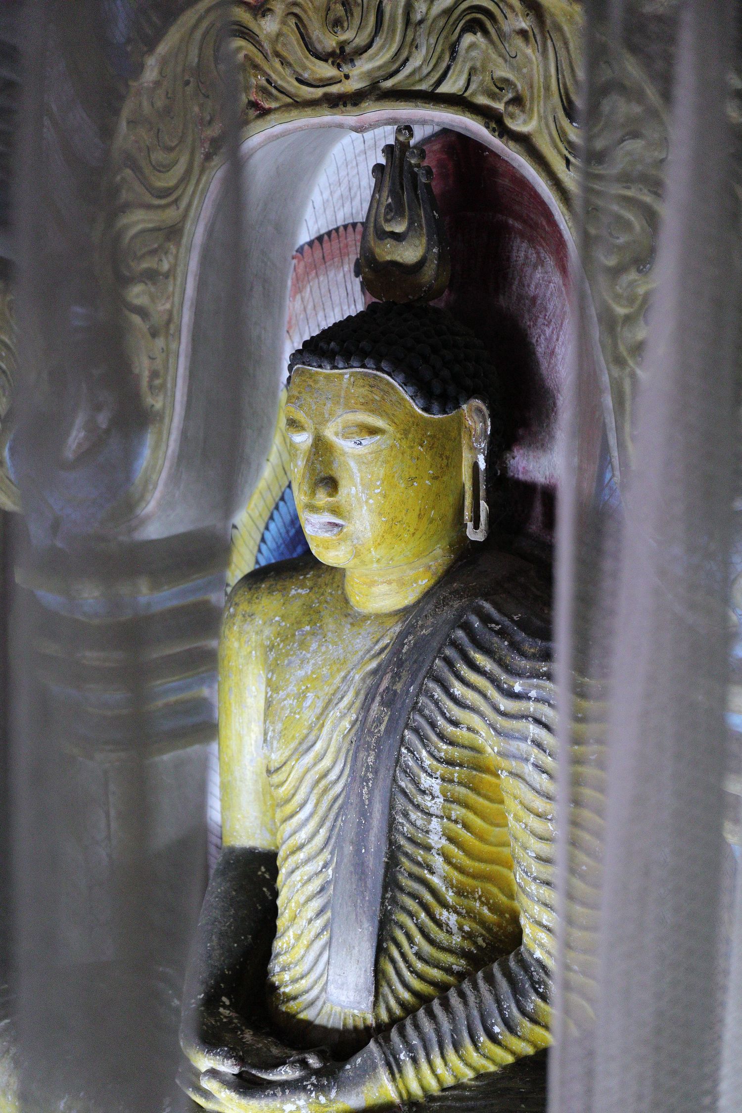 Illuminated golden Buddha statue in ornate temple alcove with detailed carving.