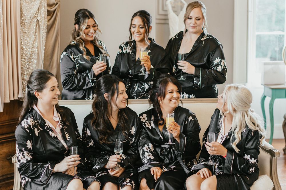 Group of bridesmaids in matching black robes laughing together.
