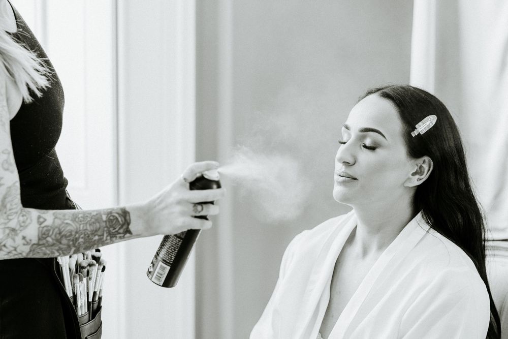 Hairspray being applied during wedding day preparation in a bright white room.