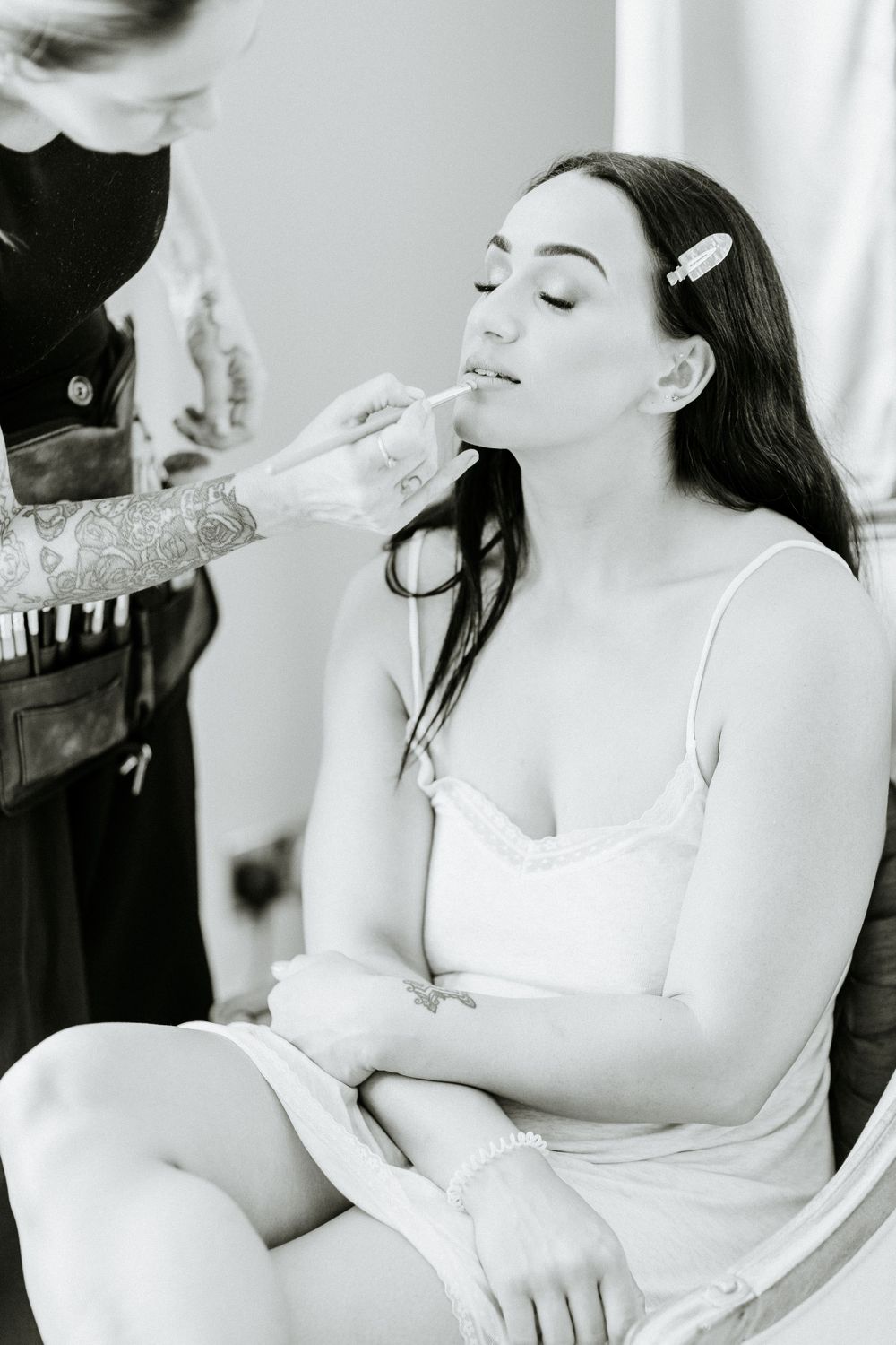 Black and white photo of bride getting makeup applied during wedding preparations.