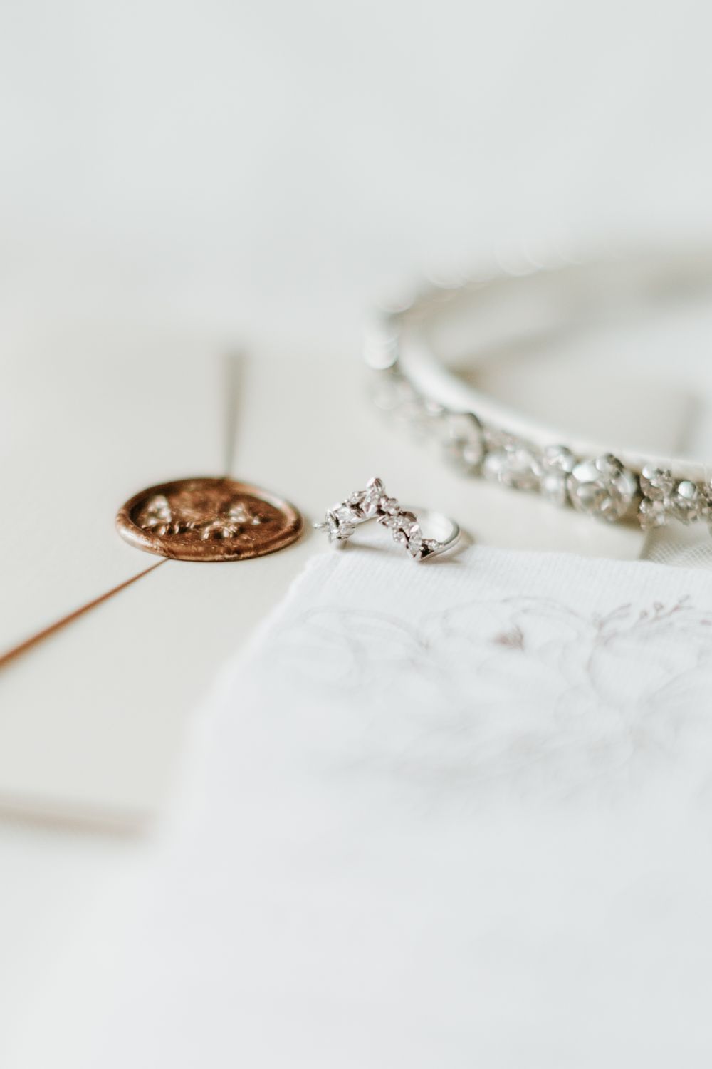 Delicate wedding jewelry and invitation details with wax seal in soft lighting.
