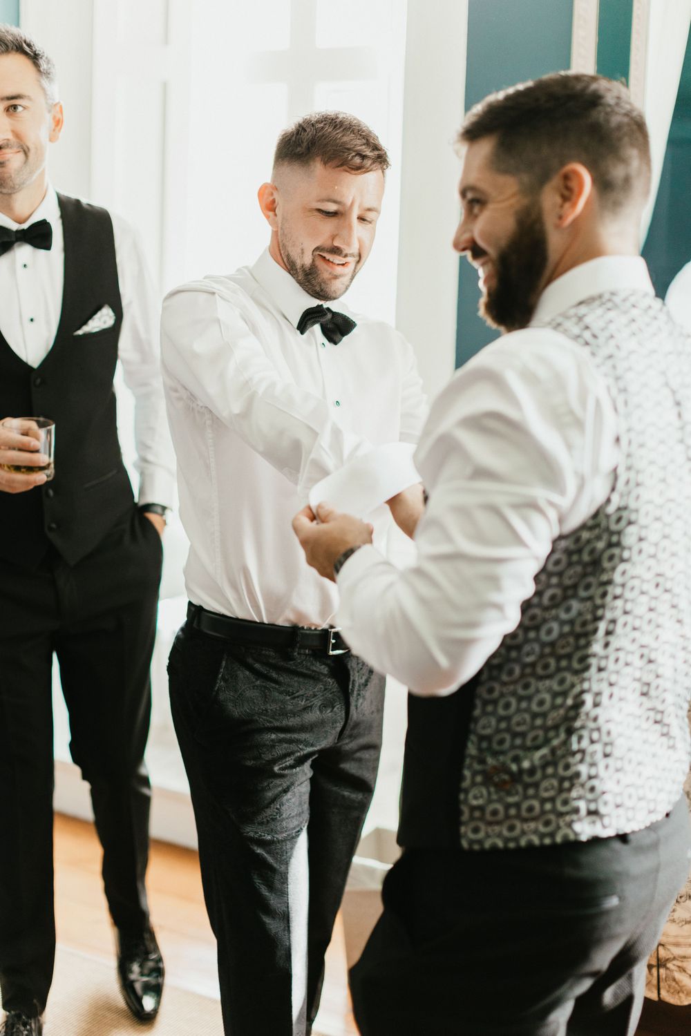 Groomsmen in formal attire sharing a laugh while getting ready.