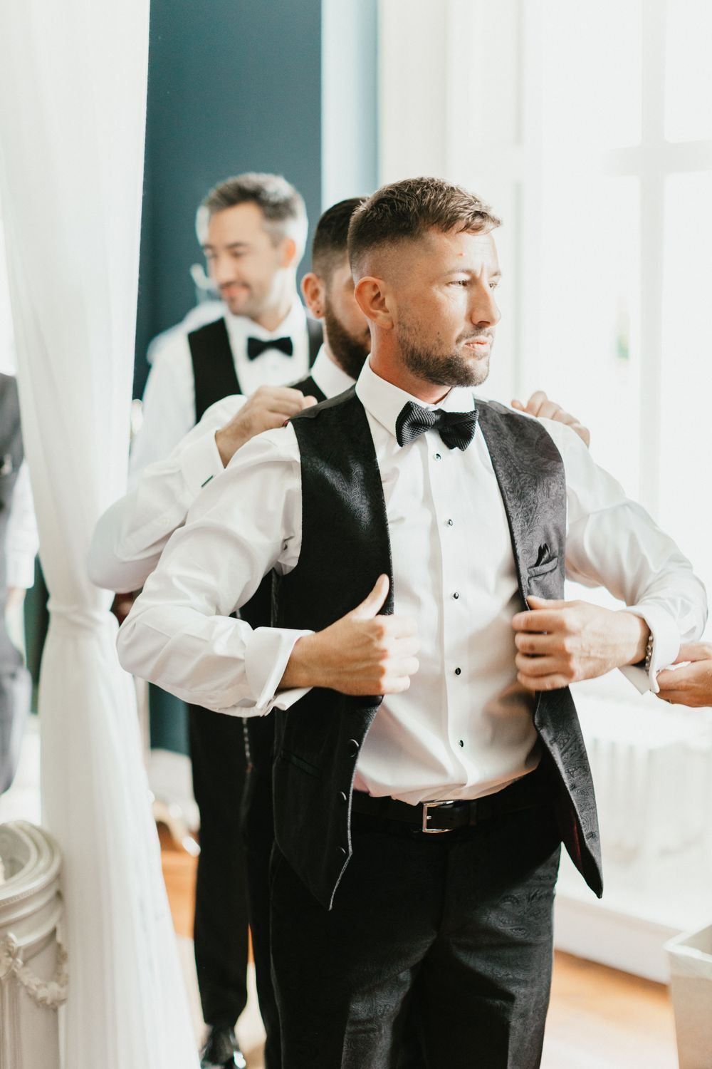 Groomsman putting on a formal black vest over white dress shirt.