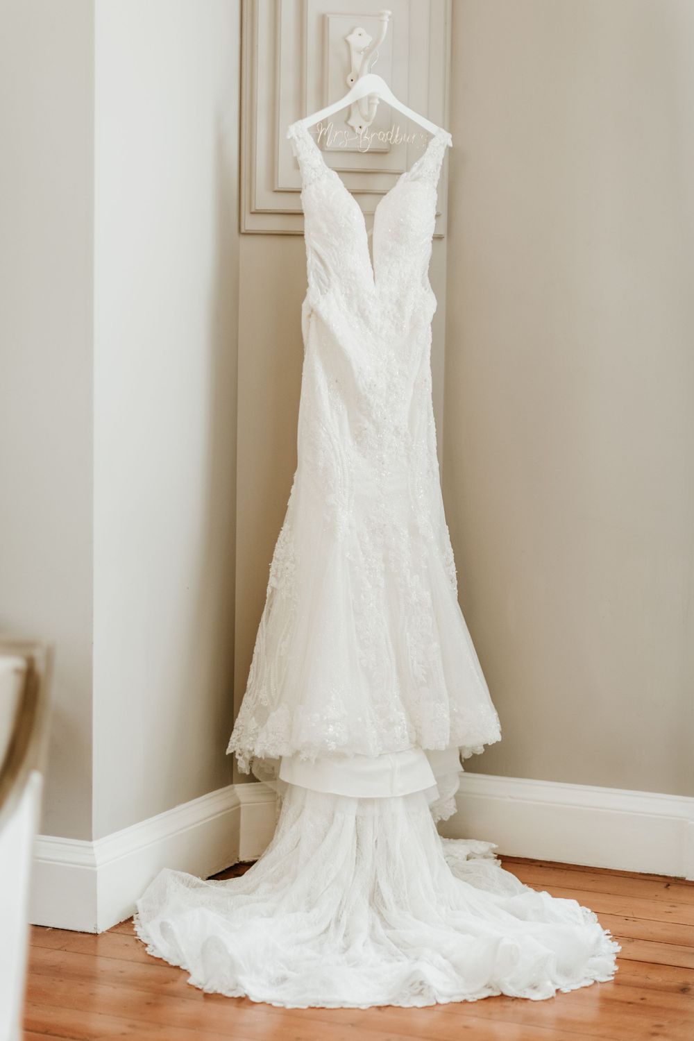 Elegant white lace wedding dress hanging on display in corner of room.