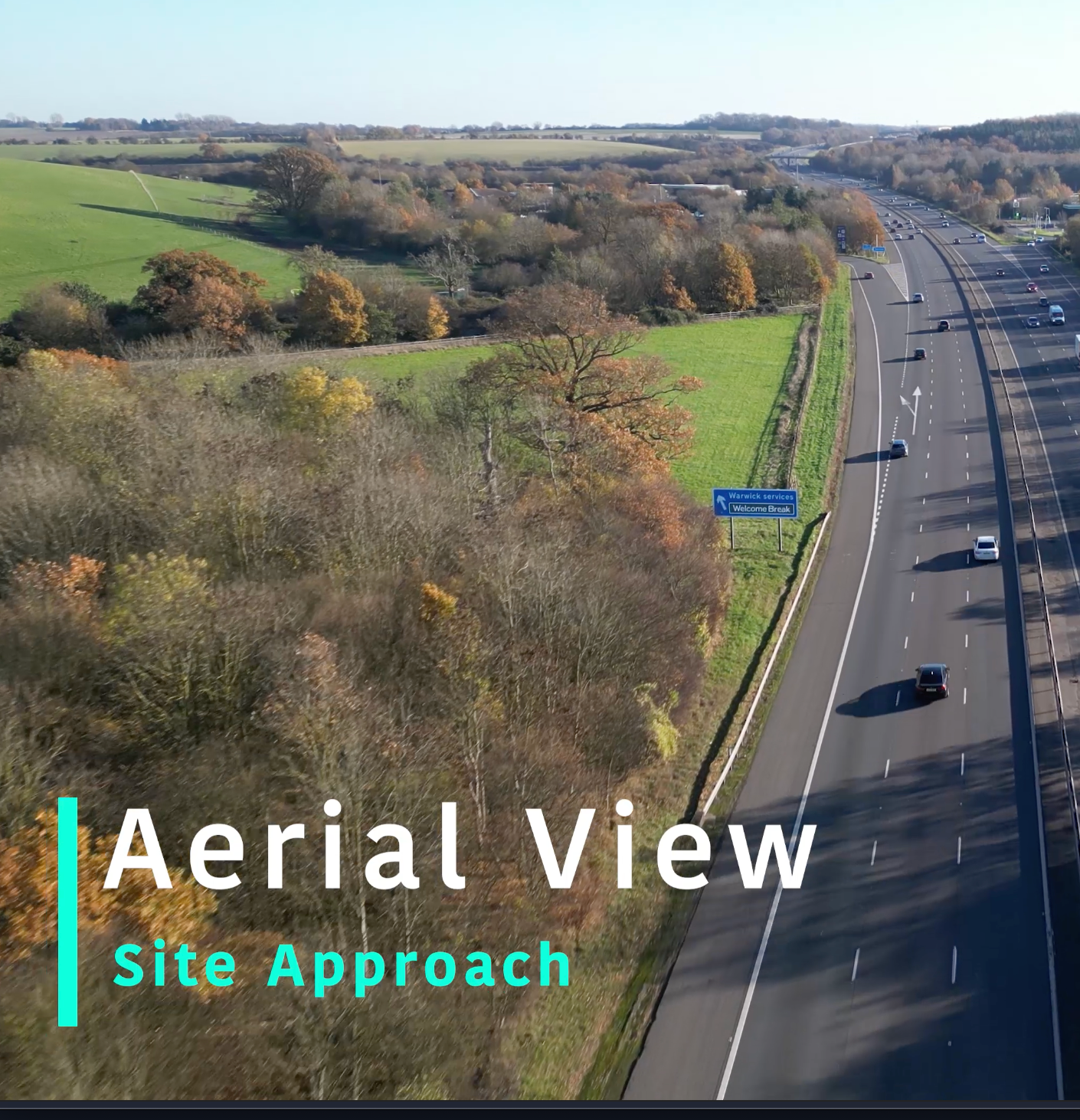 Highway aerial view showing dual carriageway with green fields and trees alongside the road.