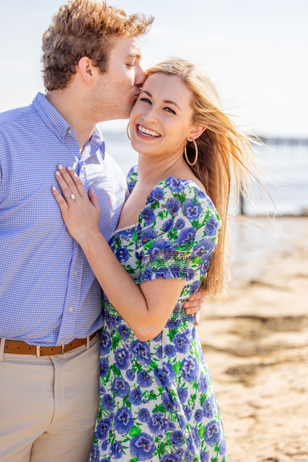 A romantic couple shares an intimate moment on the beach in summer attire.