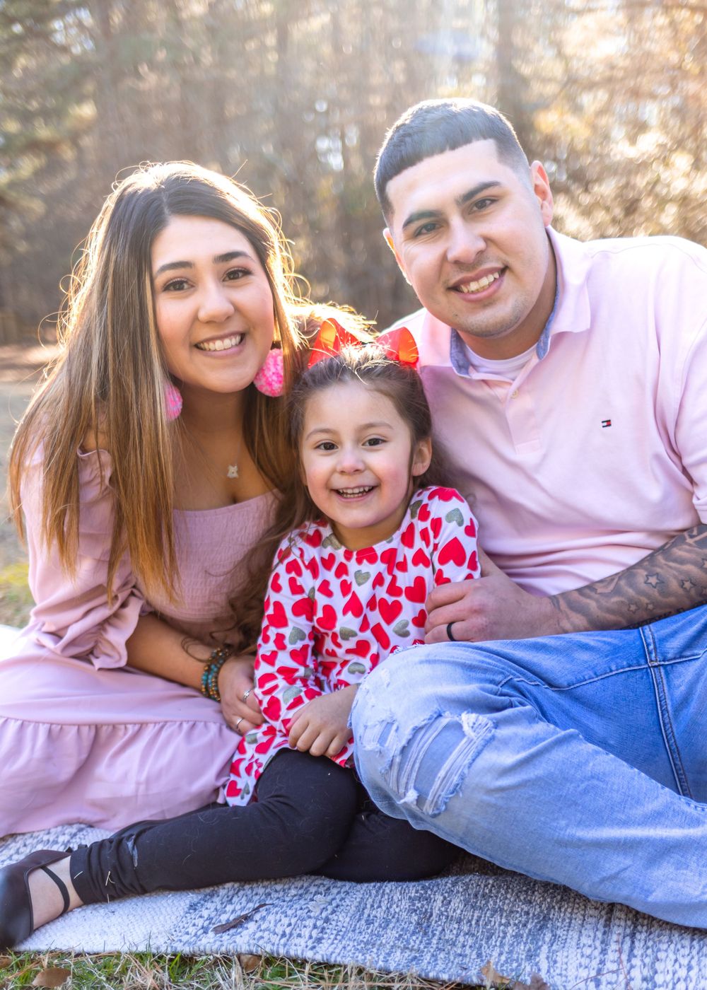 A joyful family sits together outdoors on a blanket with sunlight filtering through trees in the background.