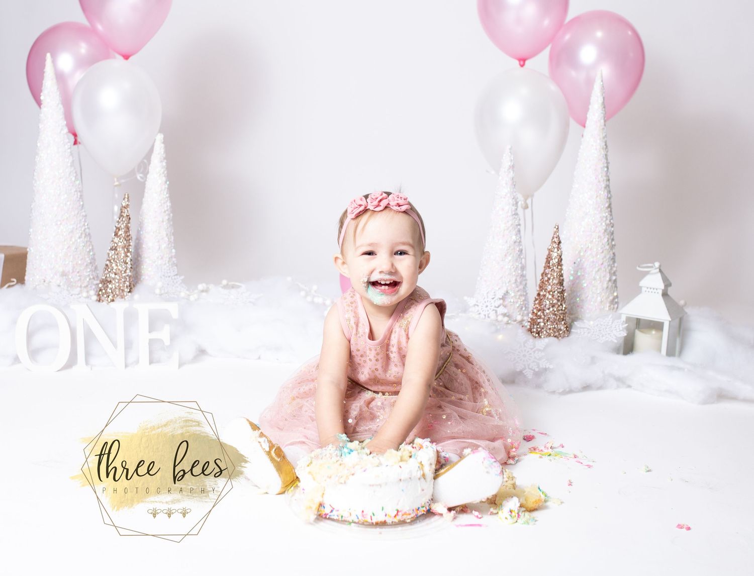 First birthday cake smash photo setup with pink decorations and balloons against white backdrop.