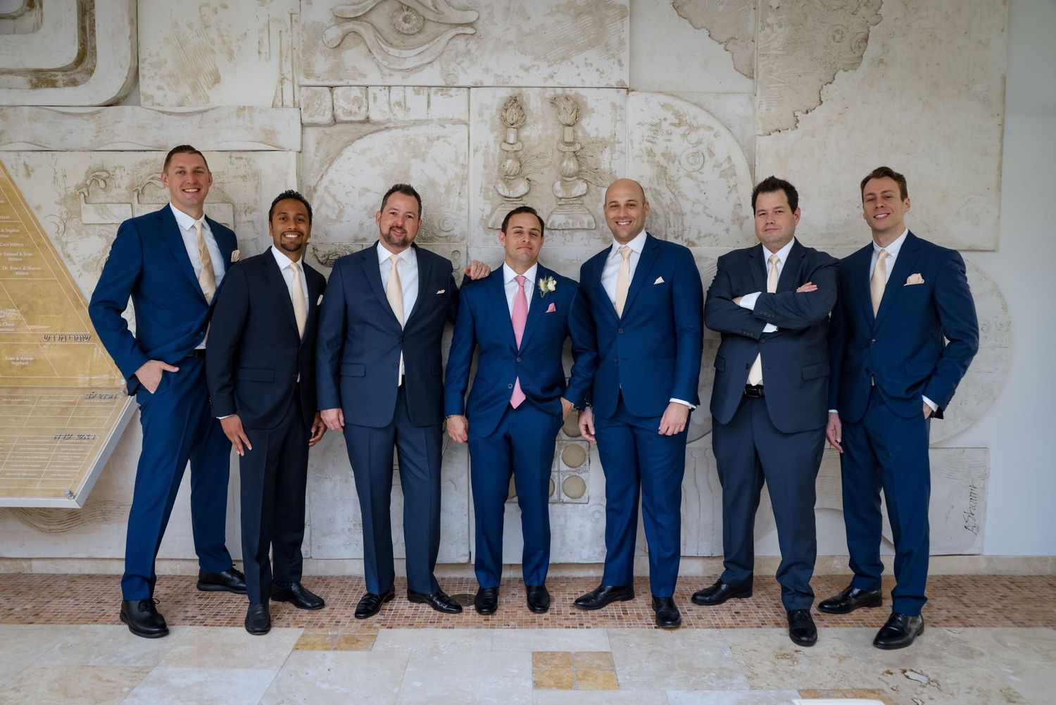 Groomsmen in coordinated navy suits pose against a textured stone wall background.