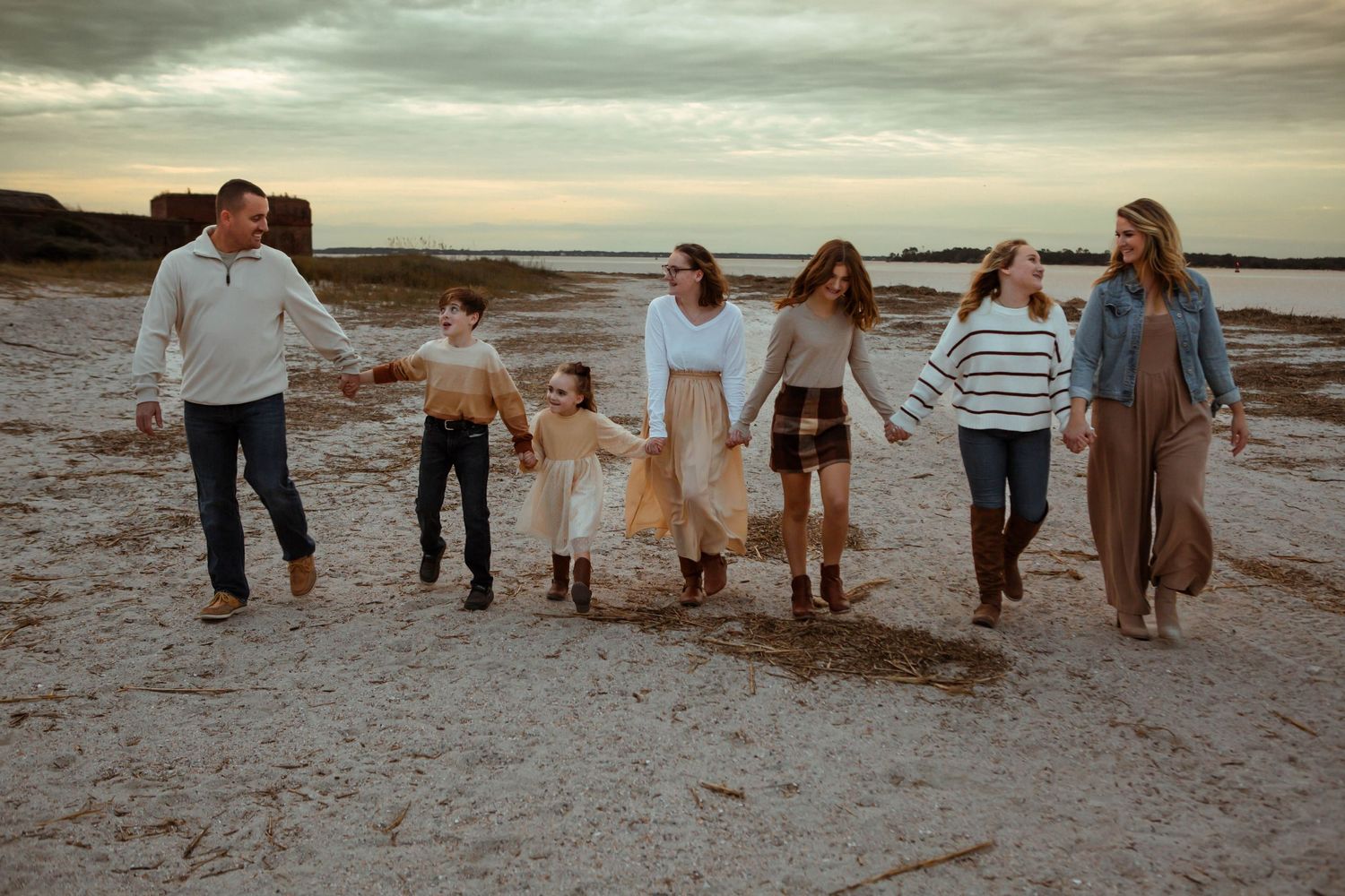Family walking together on the beach at sunset holding hands.