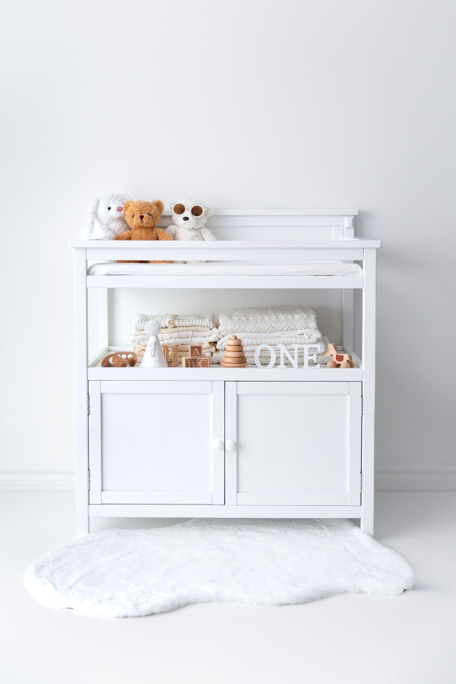 White baby change table with wooden toys and folded knits on shelf