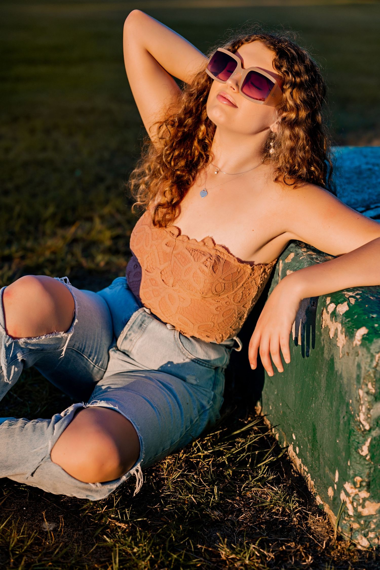 Person lounging on grass wearing pink top and jeans during sunset photoshoot.