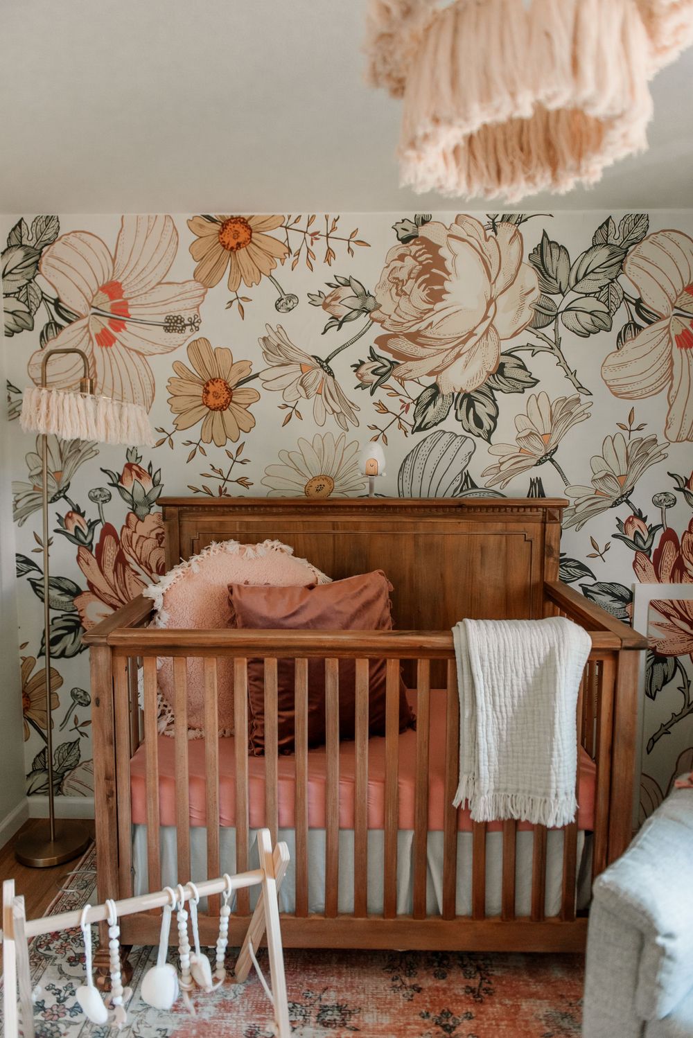 Wooden crib with floral wallpaper and peach accents in a nursery setting.