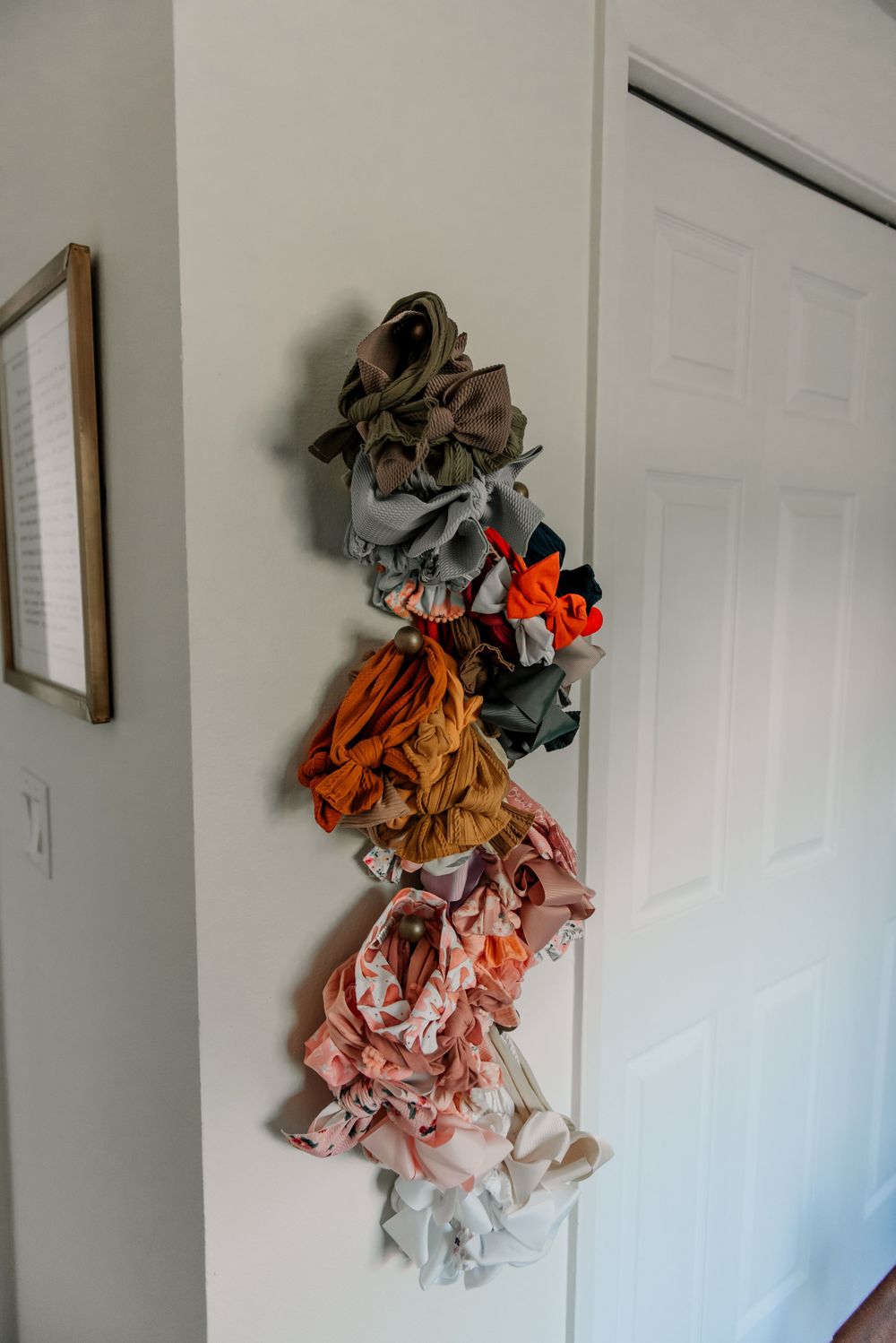 Collection of colorful baby clothes and accessories hanging on white wall hooks.