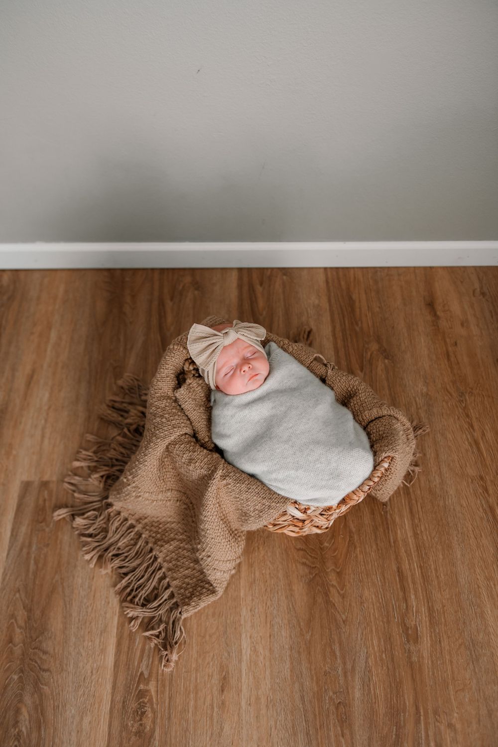 A newborn baby sleeping peacefully on a brown textured blanket against wooden flooring.