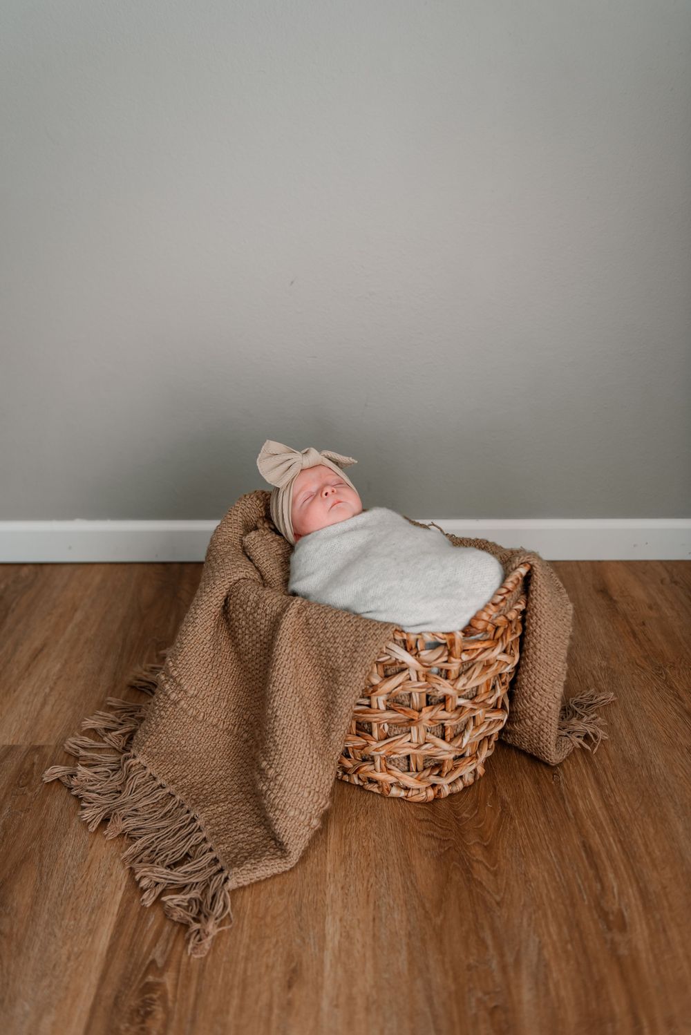 A sleeping baby wrapped in gray fabric with a bow, resting on brown textured material.