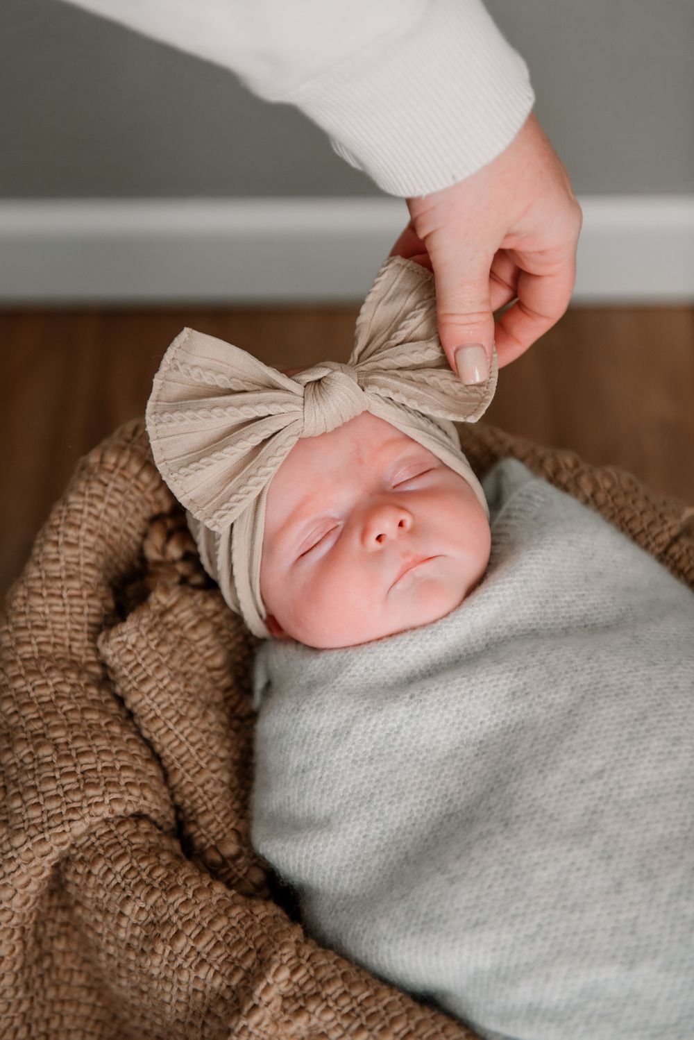 Close-up shots of a sleeping newborn with a bow headband wrapped in soft gray fabric.