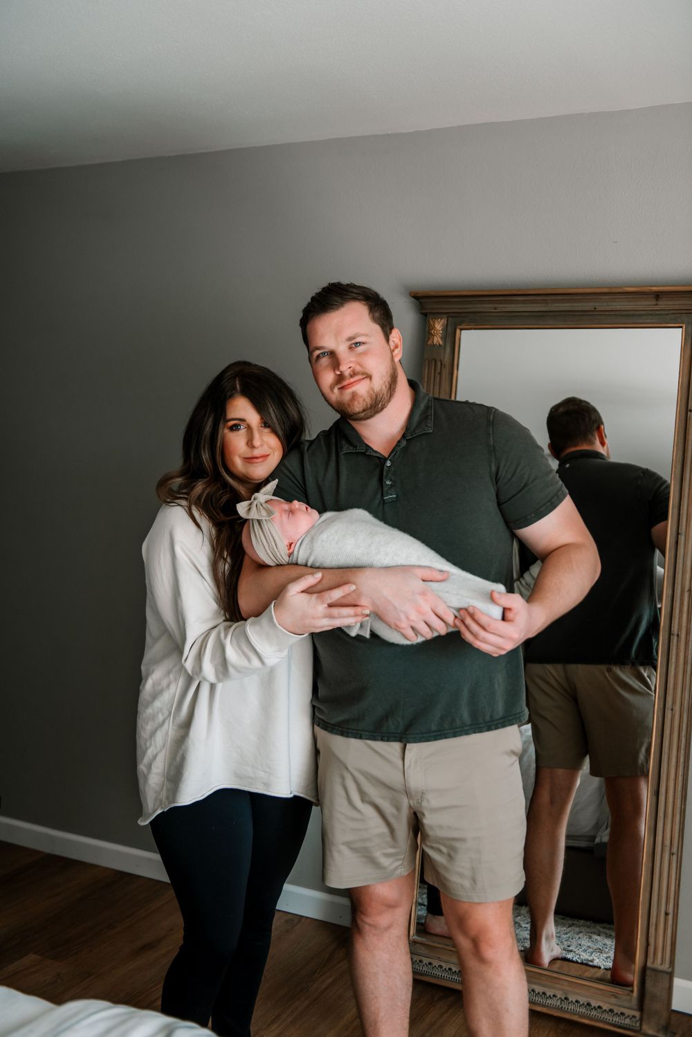 Two people share playful moments while standing next to a mirror in a bedroom.