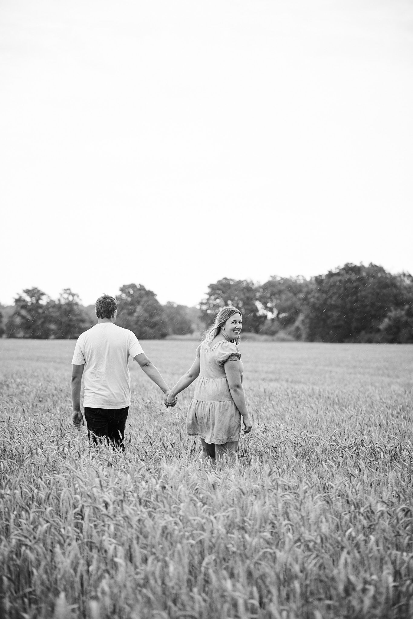A couple holding hands while walking through a wheat field in black and white.