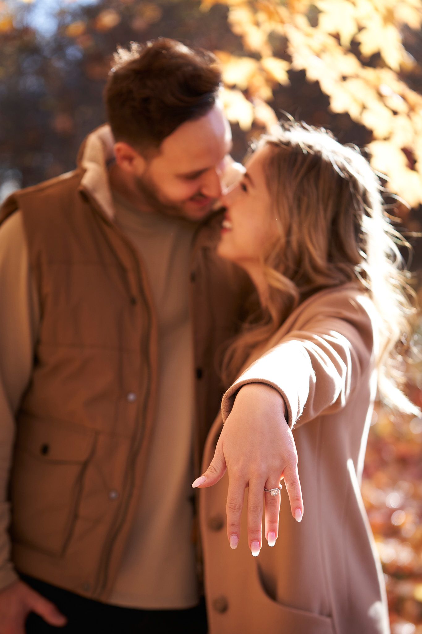 A romantic couple shares an intimate moment in autumn sunlight as she displays an engagement ring.