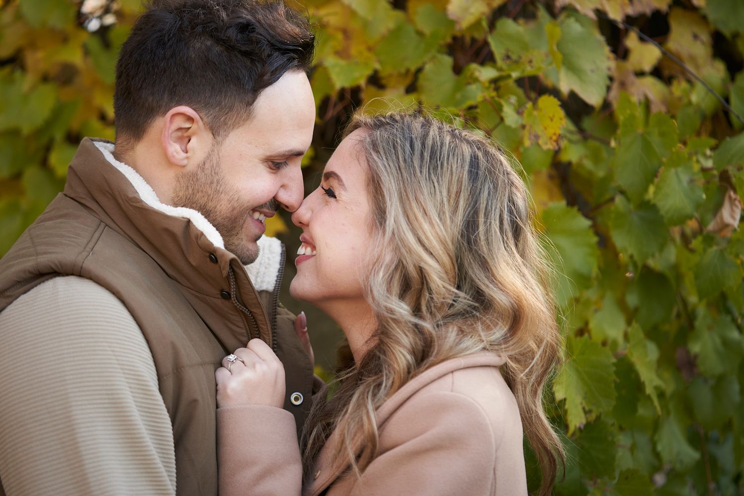 A couple shares an intimate moment among green vines during an outdoor photoshoot.
