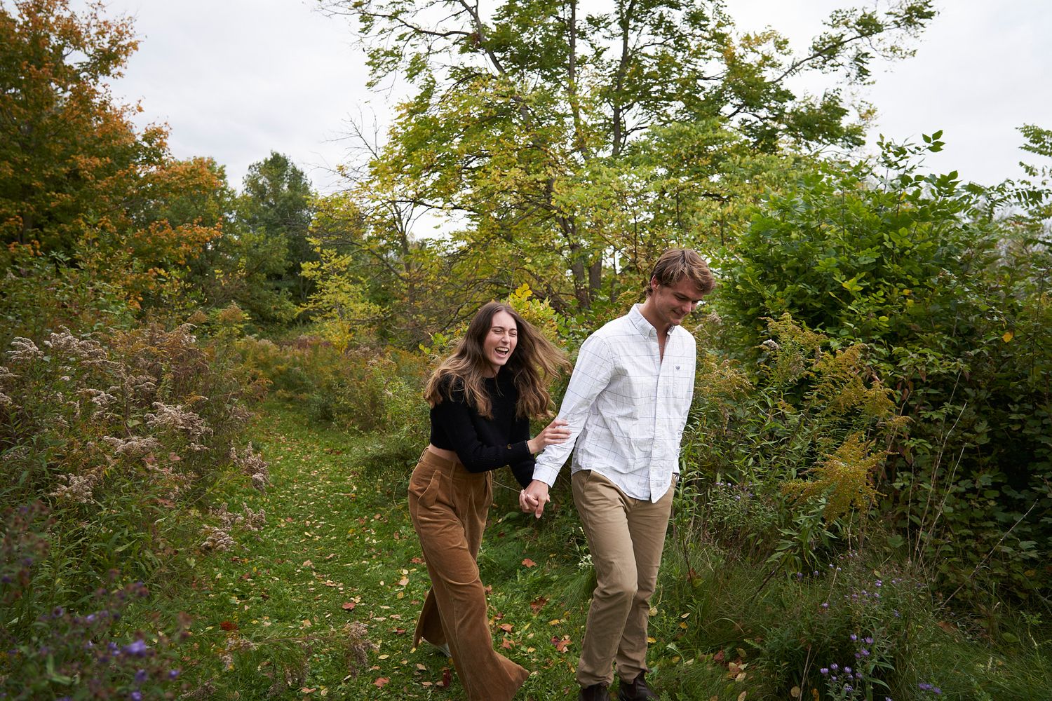 A couple walking hand in hand through a scenic autumn trail.