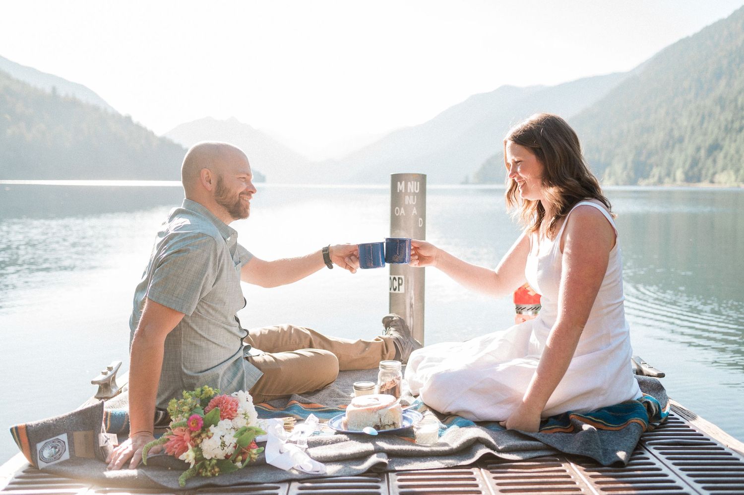 Couple toasting coffee during their Lake Crescent elopement while sitting on dock. Photo by Pine + Vow.