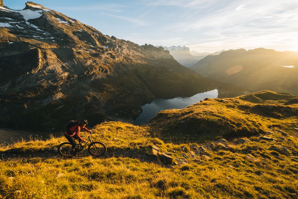 Mountain biker overlooking scenic alpine lake during golden hour in the mountains.