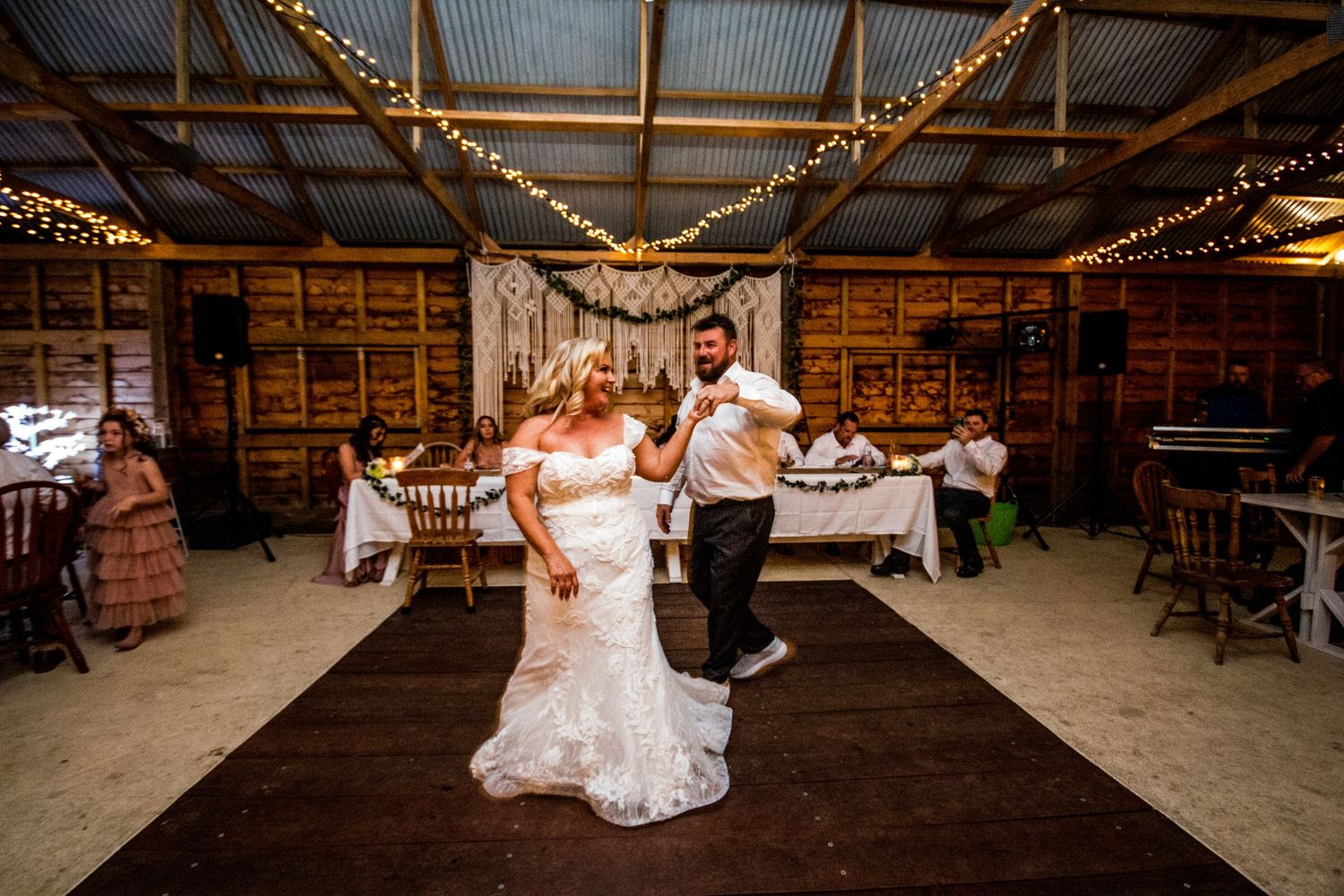 A couple dances energetically in a rustic barn venue decorated with string lights.