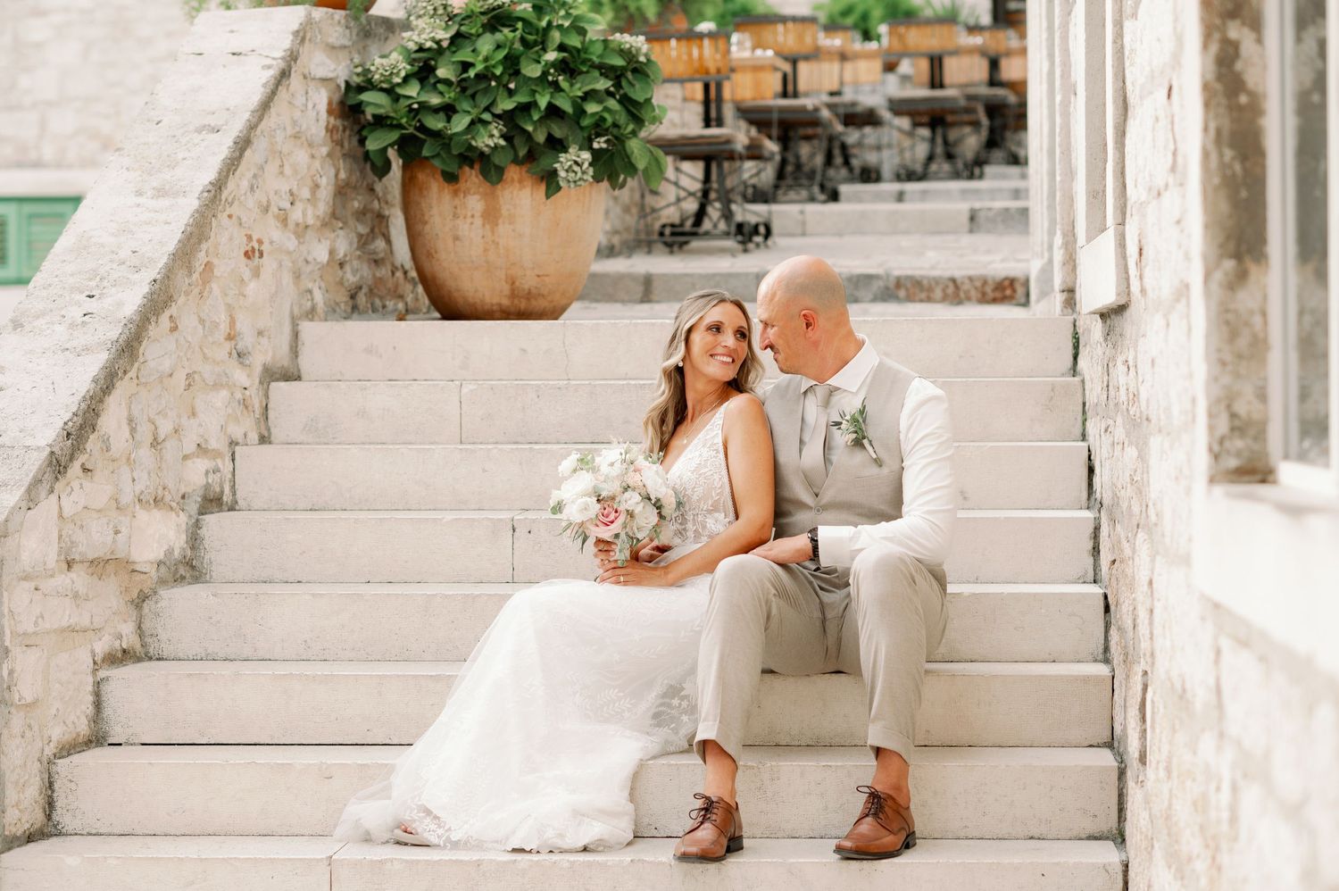 Romantic wedding moment on white stone steps with potted plants in background.