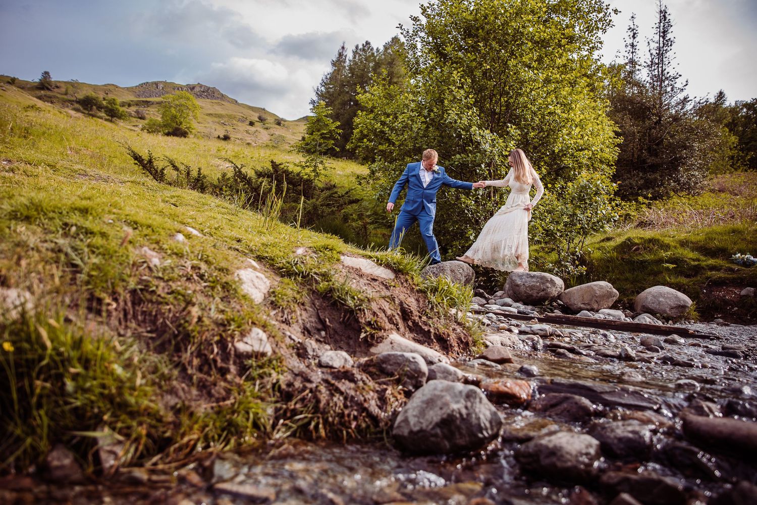 Lake District Elopement Photographer: Bride and Groom Walking over Stepping Stones at Rydal