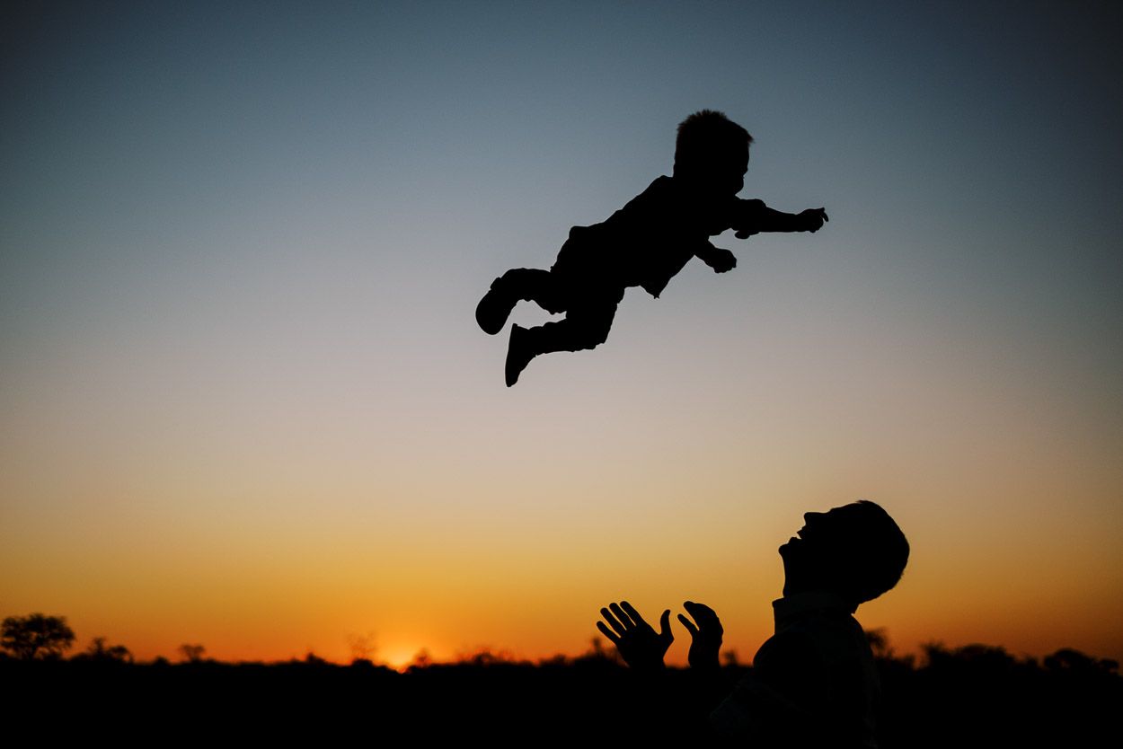 Father throws son into the air at sunset, silhouette.