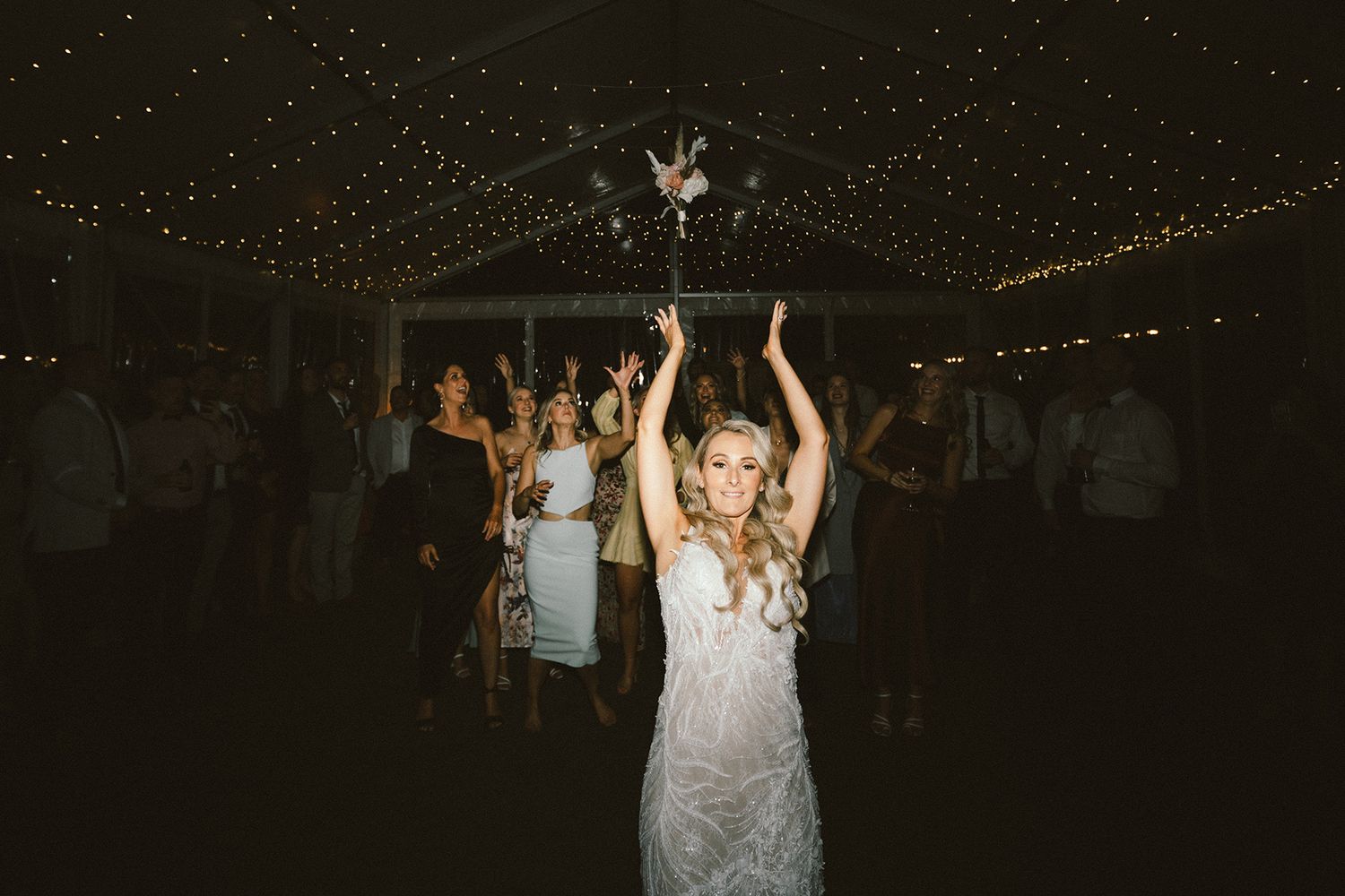 Celebratory scene on a wedding reception dance floor with festive lighting overhead.
