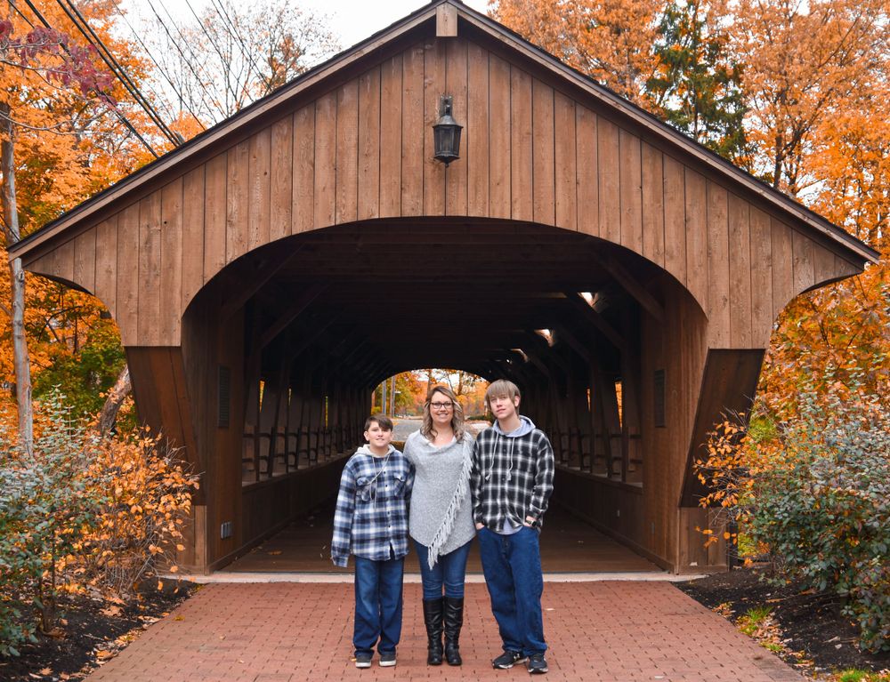Family standing together at entrance of wooden covered bridge during fall season.
